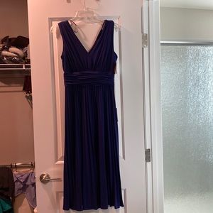 Pleated sleeveless dress color is Iris blue/purple with cumber bun look.